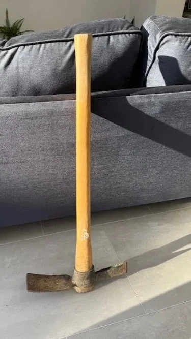 A pick axe leaning against a grey sofa