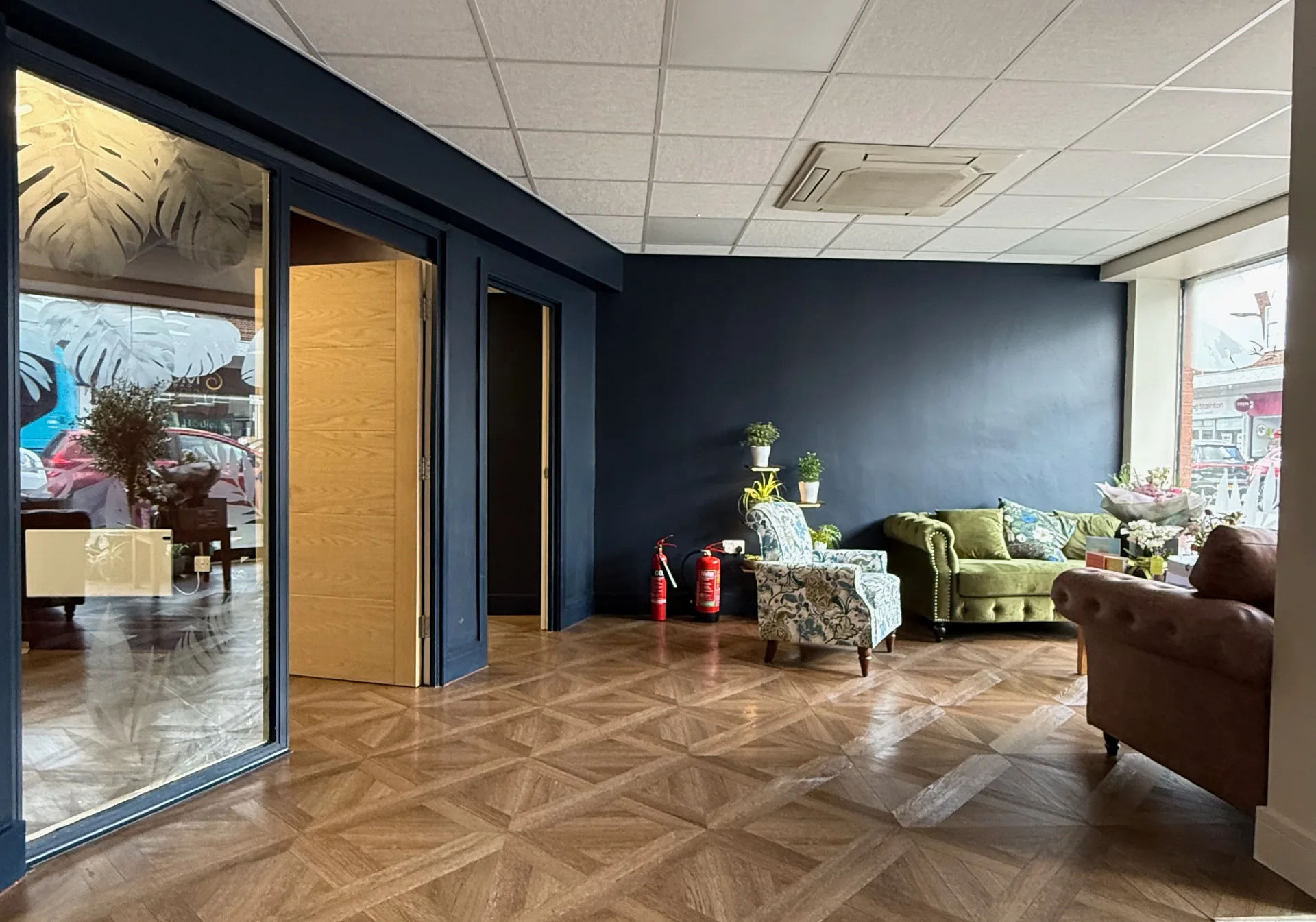 The reception area at The Wellness Lounge Leeds, with green and brown sofas against a navy wall